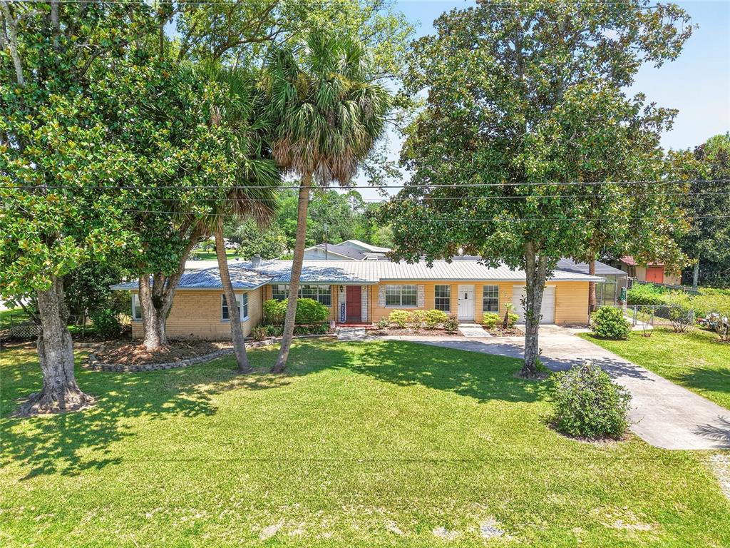 A single-story yellow brick house with a metal roof, palm trees, and a concrete driveway — 223 NW 7TH STREET, WILLISTON, FL