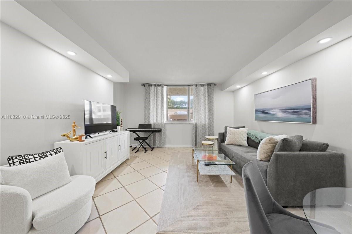 A living room features a grey sofa, white armchair, media console, and tile flooring — 540 Brickell Key Dr # 412, Miami FL 33131, MIAMI, FL