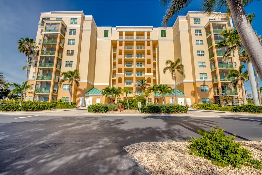 A multi-story tan apartment building with screened balconies and palm trees in the foreground — 2090 MATECUMBE KEY ROAD UNIT 1202, PUNTA GORDA, FL