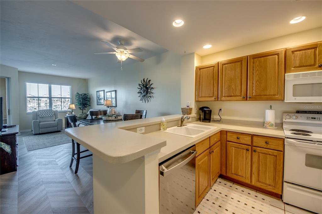 A kitchen with oak cabinets and a breakfast bar overlooks a living and dining area — 2090 MATECUMBE KEY ROAD UNIT 1202, PUNTA GORDA, FL
