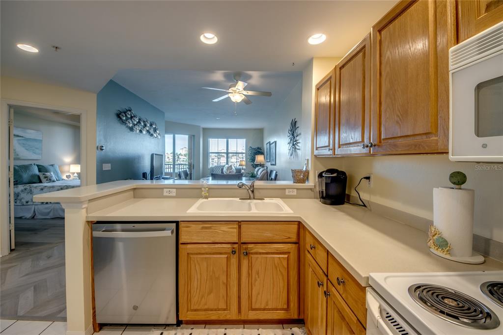 A kitchen with oak cabinets, white countertops, and stainless steel appliances overlooks a living area — 2090 MATECUMBE KEY ROAD UNIT 1202, PUNTA GORDA, FL
