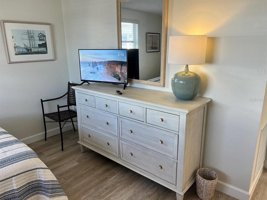 A bedroom features a light-colored wooden dresser, a television, a mirror, and a table lamp — 6020 MIDNIGHT PASS ROAD UNIT 45, SARASOTA, FL