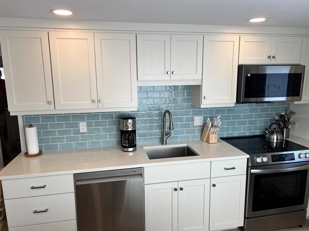 A kitchen features white cabinets, light countertops, stainless steel appliances, and a blue subway tile backsplash — 6020 MIDNIGHT PASS ROAD UNIT 45, SARASOTA, FL