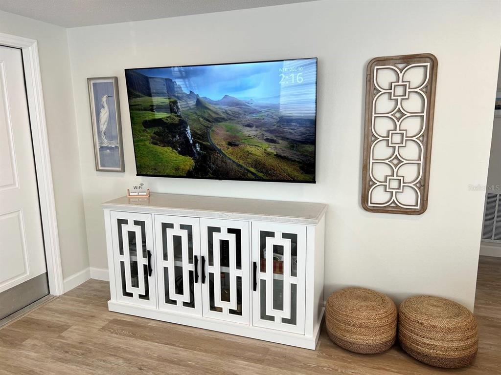 A white media console with mirrored doors sits below a wall-mounted television and wall art — 6020 MIDNIGHT PASS ROAD UNIT 45, SARASOTA, FL