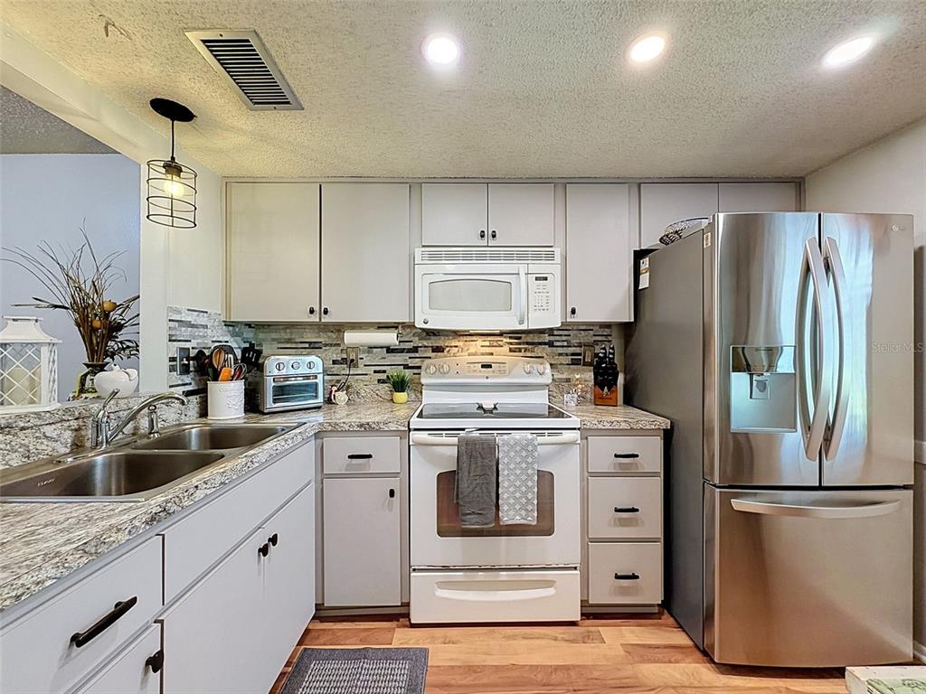 A kitchen features light gray cabinets, stainless steel appliances, and a stone tile backsplash — 8220 SEVEN OAKS COURT UNIT 5, PORT RICHEY, FL