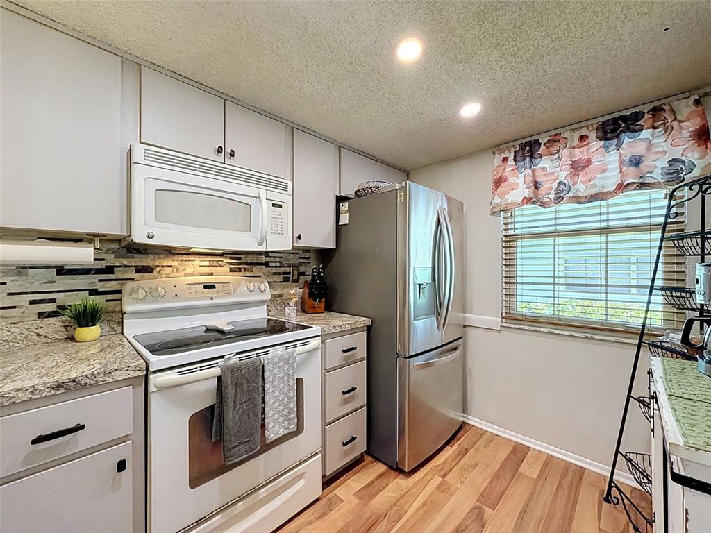 A kitchen features white cabinets, stainless steel appliances, a tiled backsplash, and wood-look flooring — 8220 SEVEN OAKS COURT UNIT 5, PORT RICHEY, FL