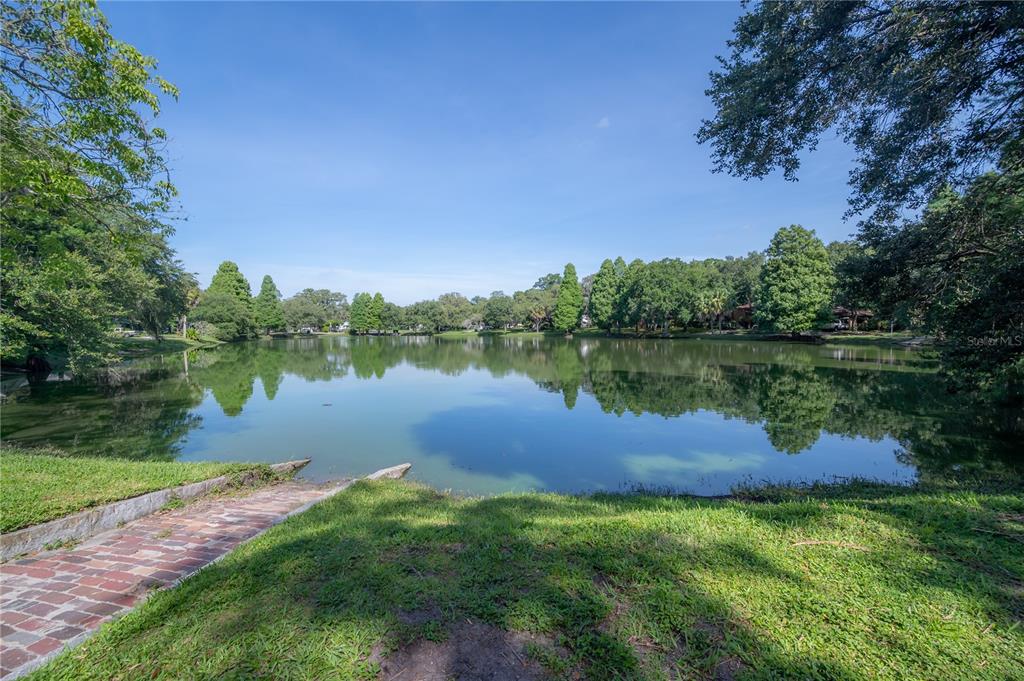 A brick walkway leads to a calm lake surrounded by lush green trees and grass — 5530 N 9TH STREET UNIT 2, TAMPA, FL