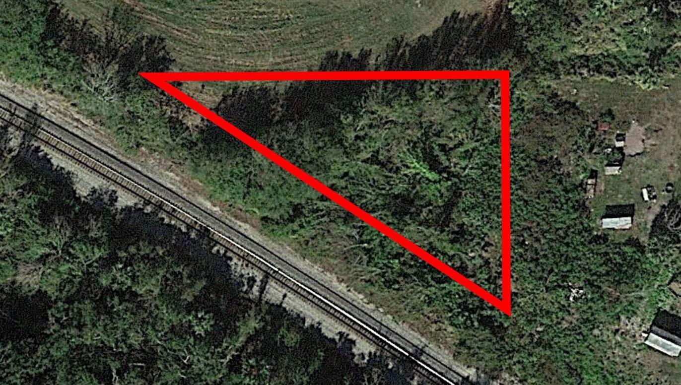 An aerial view shows a triangular plot of land bordered by railroad tracks and vegetation — 0 NE 13th Avenue, Okeechobee FL 34972, OKEECHOBEE, FL