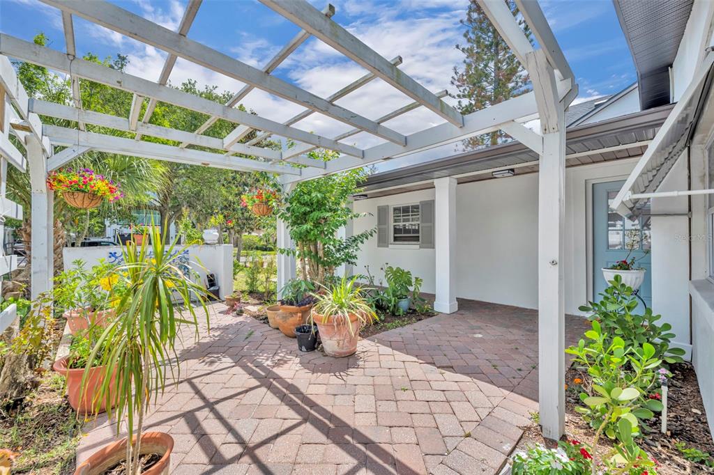 A paved patio features a white wooden pergola and potted plants against a decorative wall — 1611 CHESTNUT AVENUE, WINTER PARK, FL