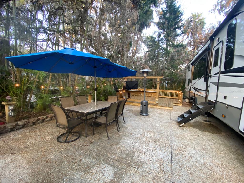 An outdoor patio features a dining set under a blue umbrella, a deck, and an RV — 313 GATOR ALLEY, LAKE WALES, FL