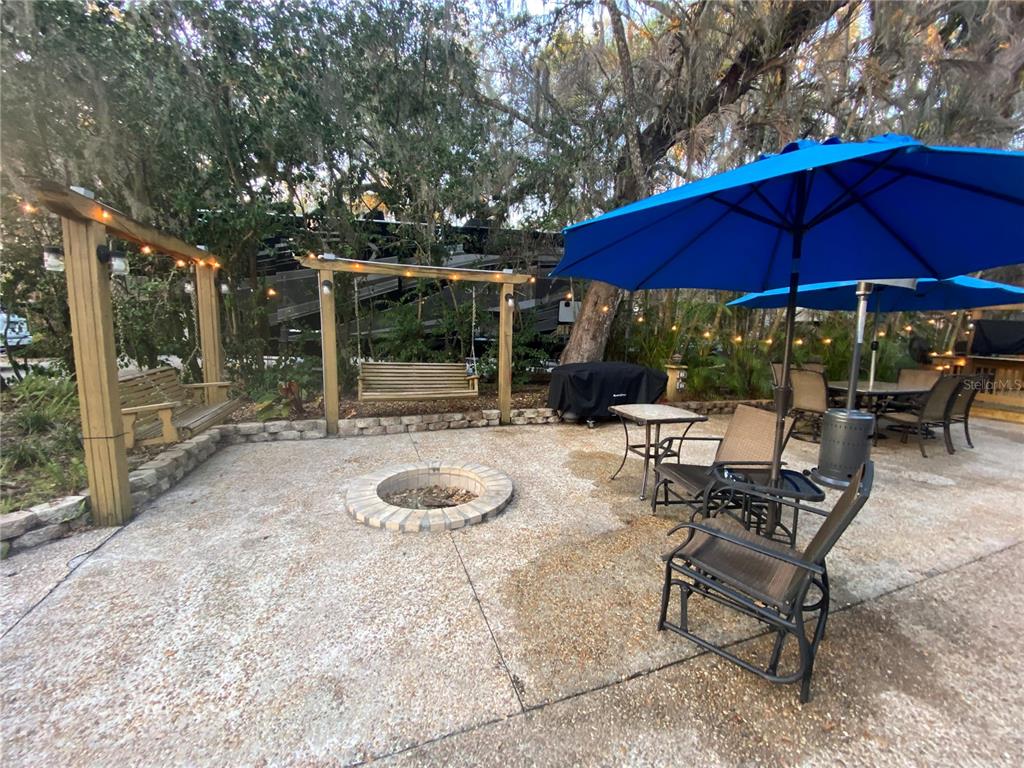 A concrete patio features a fire pit, two wooden swings, and outdoor dining furniture — 313 GATOR ALLEY, LAKE WALES, FL