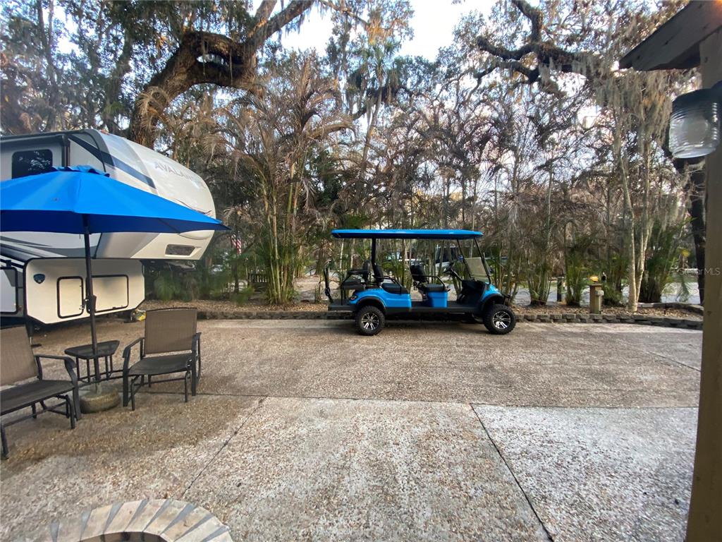 A paved patio features a blue umbrella, outdoor chairs, a parked golf cart, and an RV — 313 GATOR ALLEY, LAKE WALES, FL