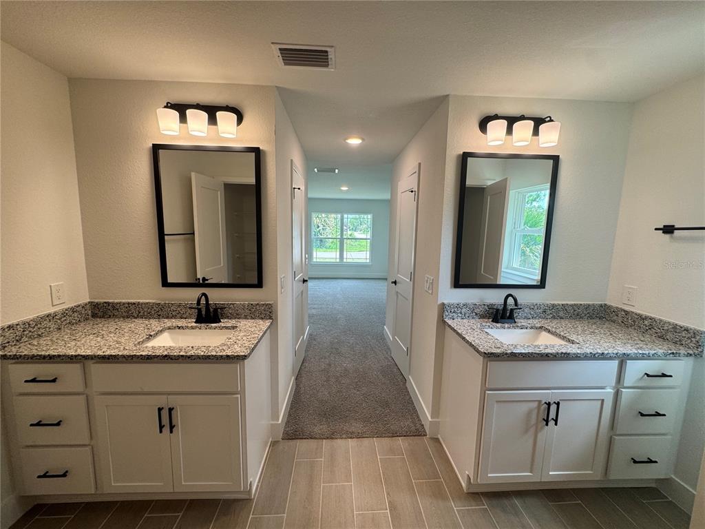 A bathroom with dual white vanities, granite countertops, black fixtures, and a carpeted hallway beyond — 5923 GIFFEN AVENUE, NORTH PORT, FL