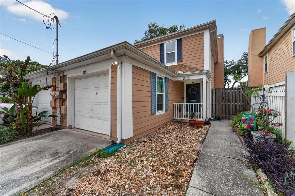 A two-story tan house with a single-car garage, gravel yard, and a small front porch — 3219 W SANTIAGO STREET UNIT B, TAMPA, FL