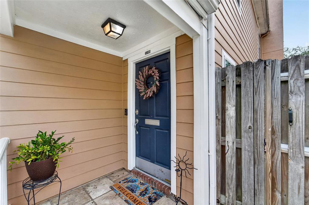 A blue front door with a wreath sits under a covered porch with tan siding — 3219 W SANTIAGO STREET UNIT B, TAMPA, FL