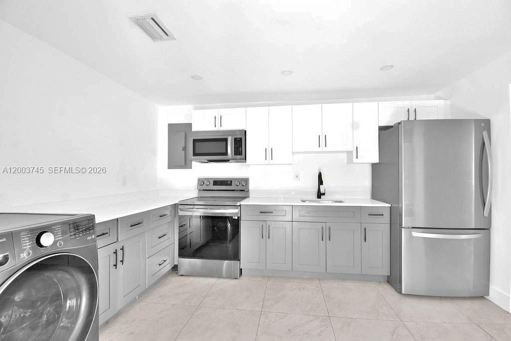A kitchen features gray lower cabinets, white upper cabinets, stainless steel appliances, and tile flooring — 1102 NW 103rd St # 1, Miami FL 33150, MIAMI, FL