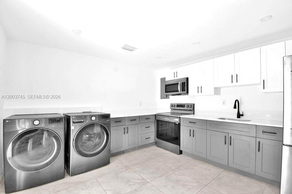A laundry room and kitchen combination featuring gray lower cabinets, white upper cabinets, and appliances — 1102 NW 103rd St # 1, Miami FL 33150, MIAMI, FL