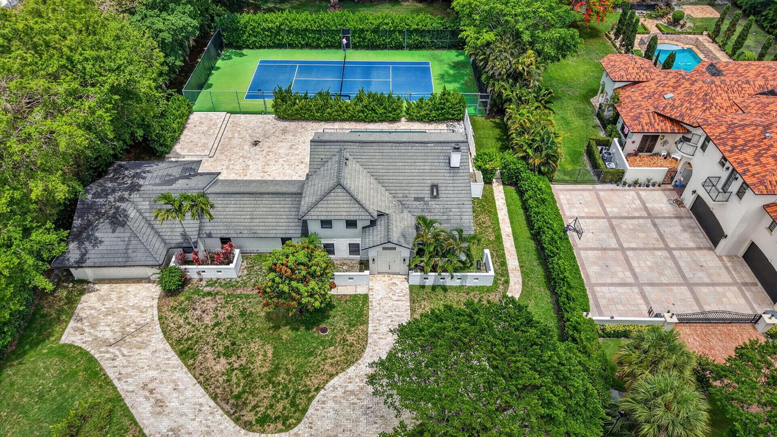 An aerial view of a house with a gray roof, tennis court, and paved driveway — 8044 Twin Lake Drive, Boca Raton FL 33496, BOCA RATON, FL