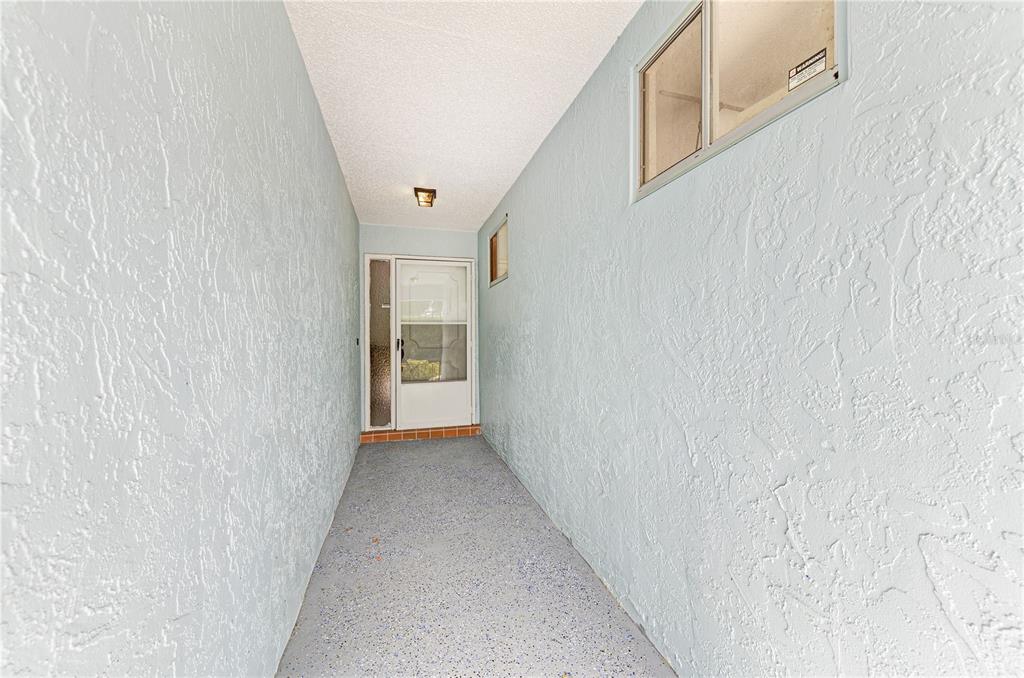 A narrow, covered entryway features light blue textured walls, a gray floor, and a white door — 804 67TH STREET W, BRADENTON, FL