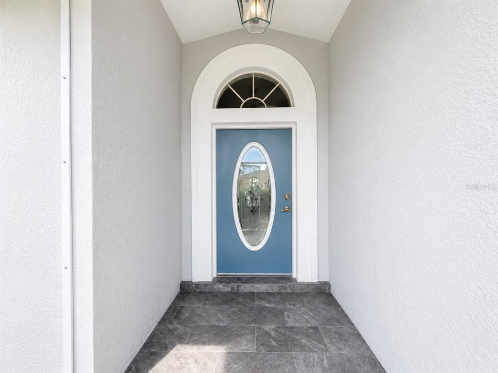 A blue front door with an oval glass insert sits within a white arched entryway — 25264 PADRE LANE, PUNTA GORDA, FL