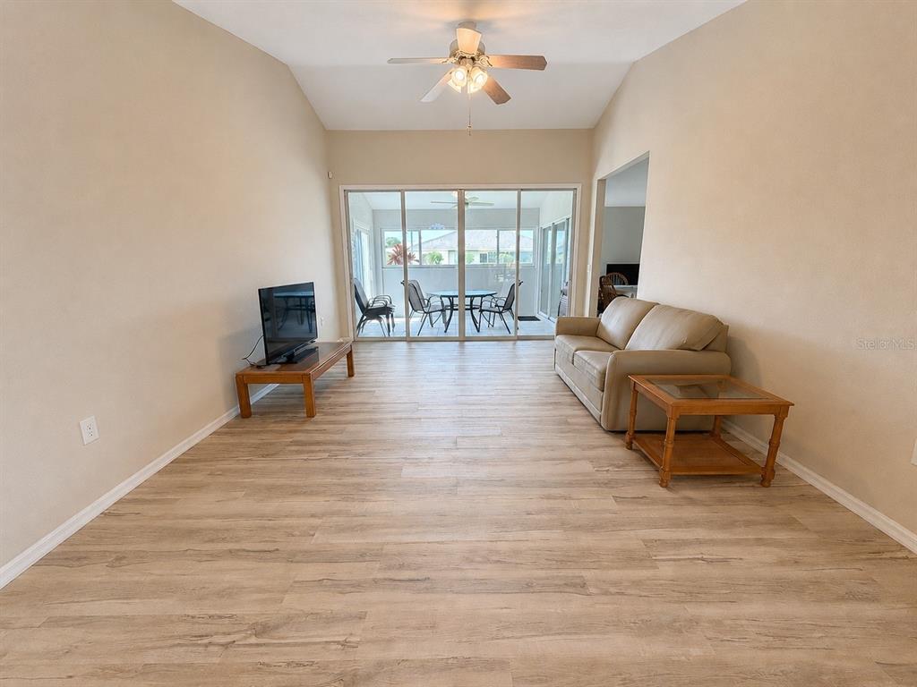 A living room features light wood-look flooring, a vaulted ceiling, and sliding glass doors — 25264 PADRE LANE, PUNTA GORDA, FL