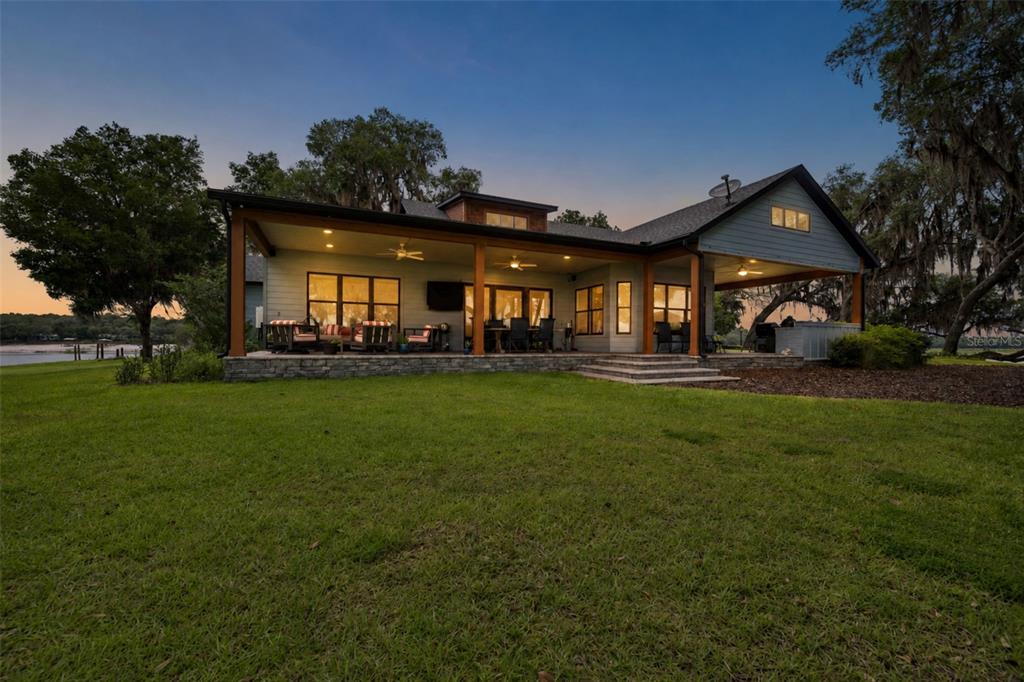 A rear view of a house with a large covered patio overlooking a grassy lawn — 7229 PLEASANT POINT ROAD, KEYSTONE HEIGHTS, FL
