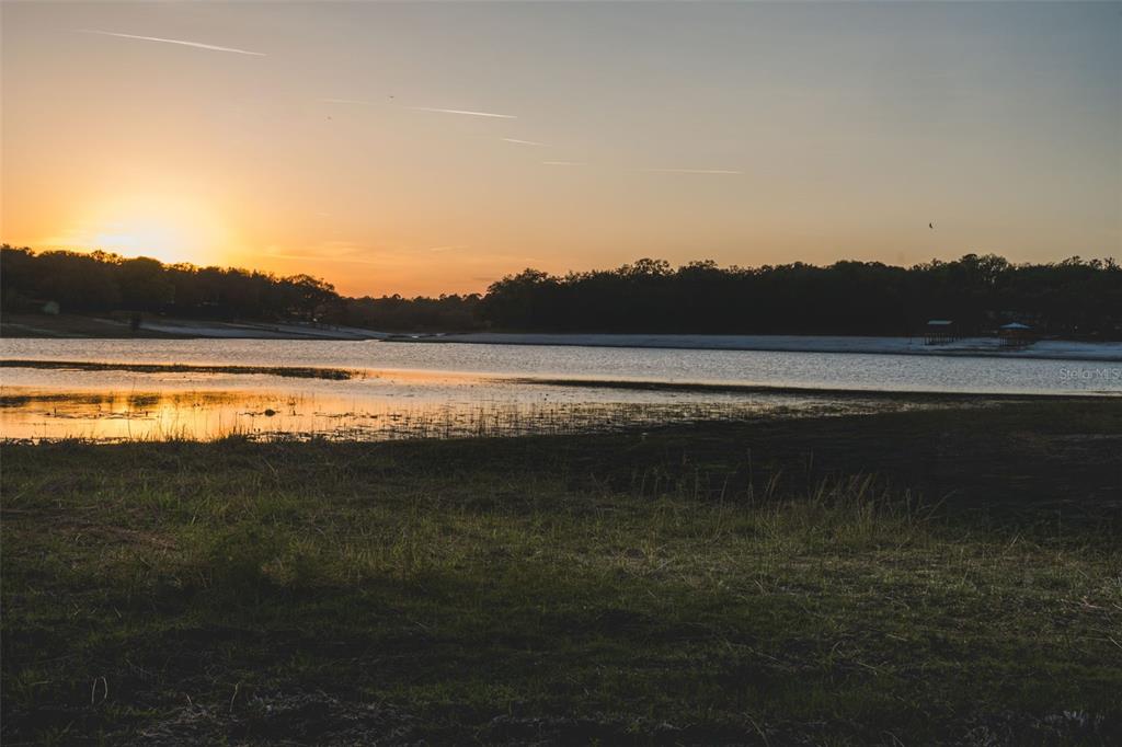 A sunset view over a lake with grassy foreground and a distant treeline — 7229 PLEASANT POINT ROAD, KEYSTONE HEIGHTS, FL