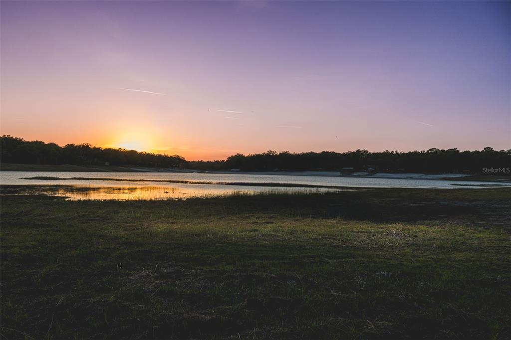 A sunset view over a grassy field leading to a lake with a treeline beyond — 7229 PLEASANT POINT ROAD, KEYSTONE HEIGHTS, FL