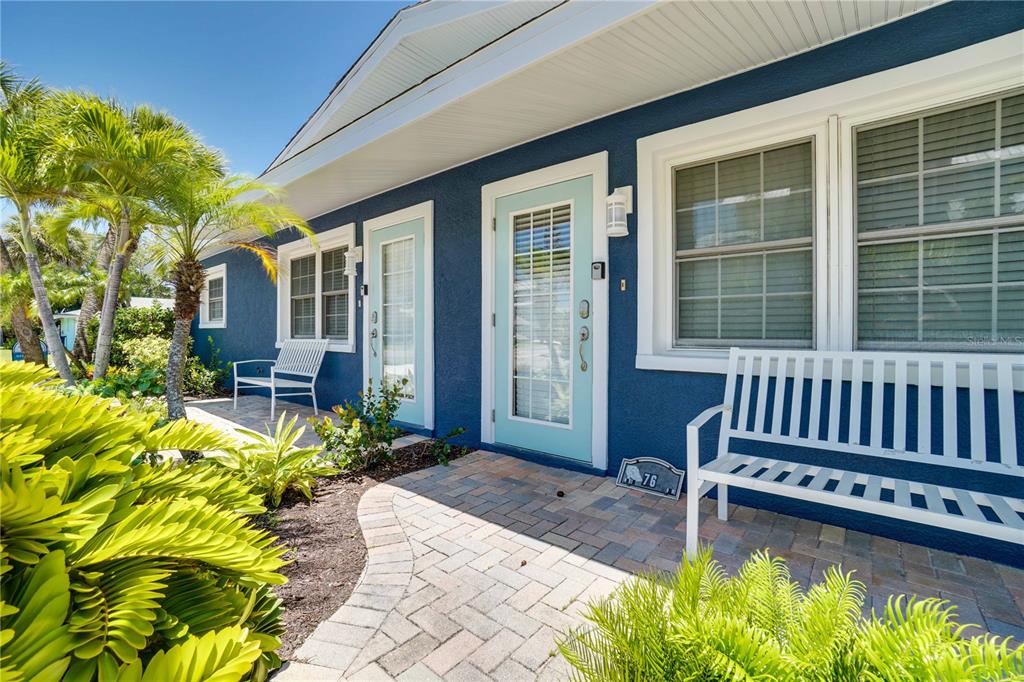 A blue exterior house features two light blue doors, white benches, and a brick walkway — 76 N SHORE DRIVE, ANNA MARIA, FL