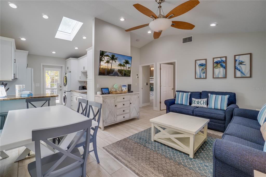 A bright living room and dining area features a blue sofa, white furniture, and skylights — 76 N SHORE DRIVE, ANNA MARIA, FL