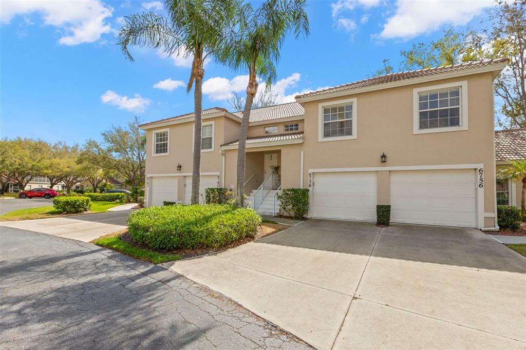A two-story residential building with beige stucco walls, multiple garage doors, and palm trees — 6758 FAIRVIEW TERRACE, BRADENTON, FL