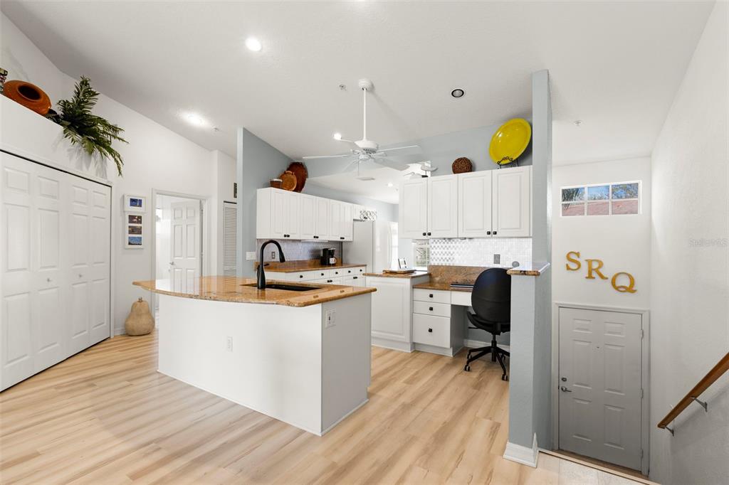 A kitchen features white cabinetry, a granite-topped island, light wood flooring, and a built-in desk — 6758 FAIRVIEW TERRACE, BRADENTON, FL