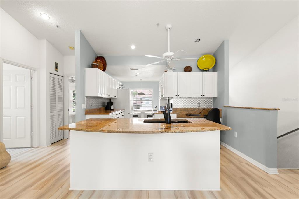 A kitchen features a granite-topped island, white cabinetry, and light wood-look flooring — 6758 FAIRVIEW TERRACE, BRADENTON, FL