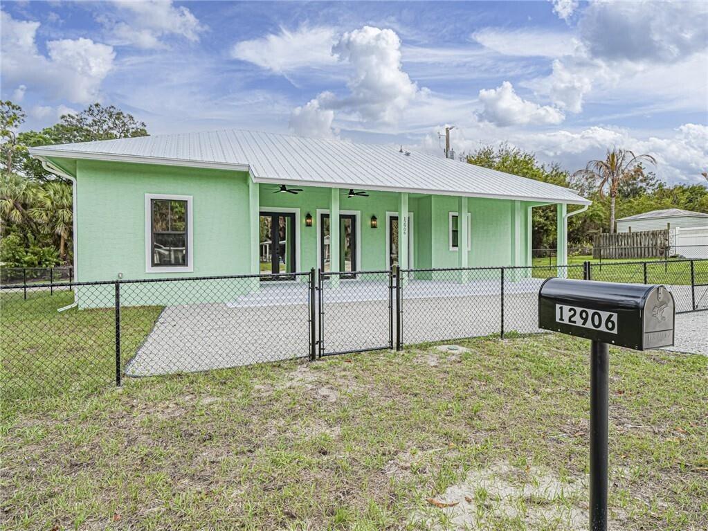 A light green house with a metal roof and a covered porch behind a fence — 12906 83rd Avenue, Sebastian FL 32958, SEBASTIAN, FL