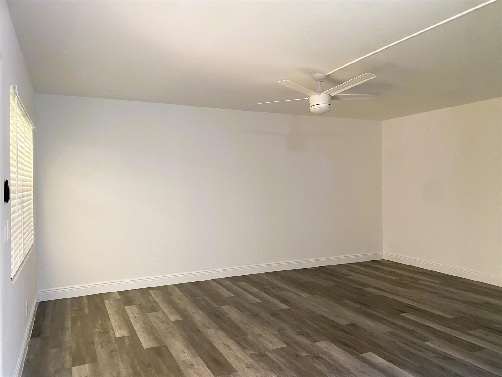 An empty room features white walls, a ceiling fan, and wood-look vinyl plank flooring — 256 Mansfield # G, Boca Raton FL 33434, BOCA RATON, FL