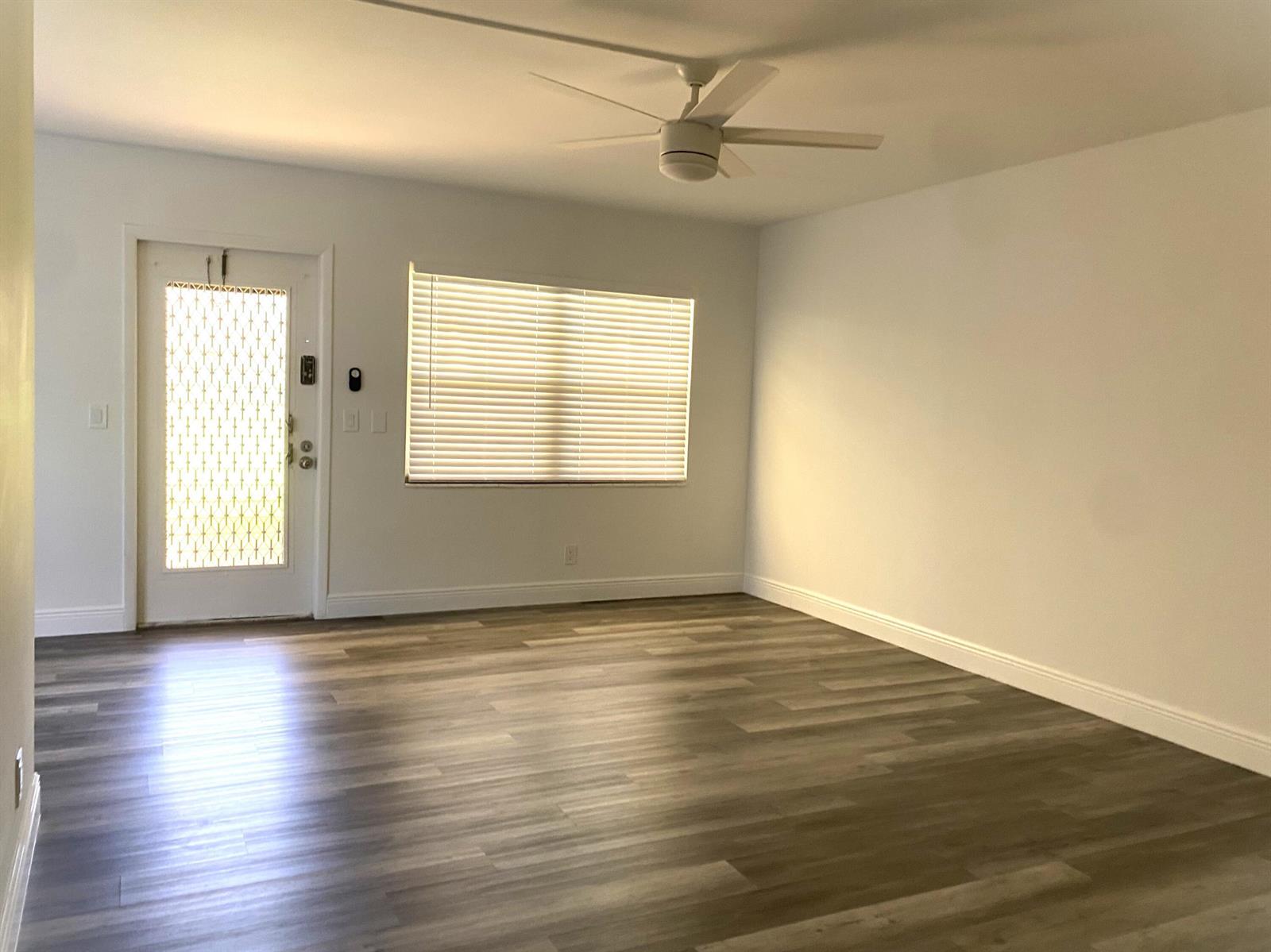 An empty room features wood-look flooring, a ceiling fan, a window with blinds, and a door — 256 Mansfield # G, Boca Raton FL 33434, BOCA RATON, FL