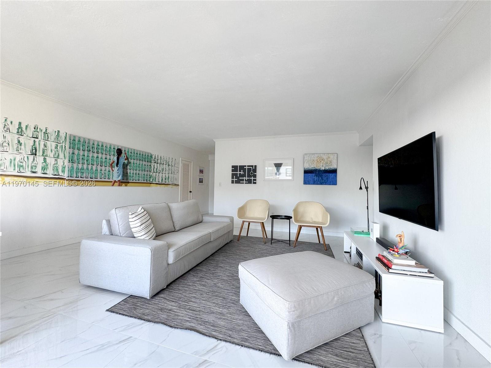 A living room features a gray sofa, a large ottoman, and a wall-mounted television — 555 Crandon Blvd # 82, Key Biscayne FL 33149, KEY BISCAYNE, FL