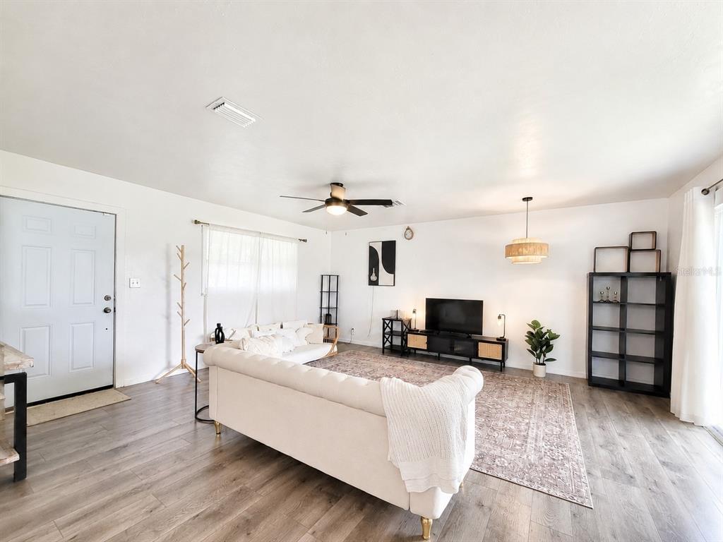 A living room features light wood-look flooring, a white sofa, a television, and shelving units — 2524 NE 5TH PLACE, GAINESVILLE, FL