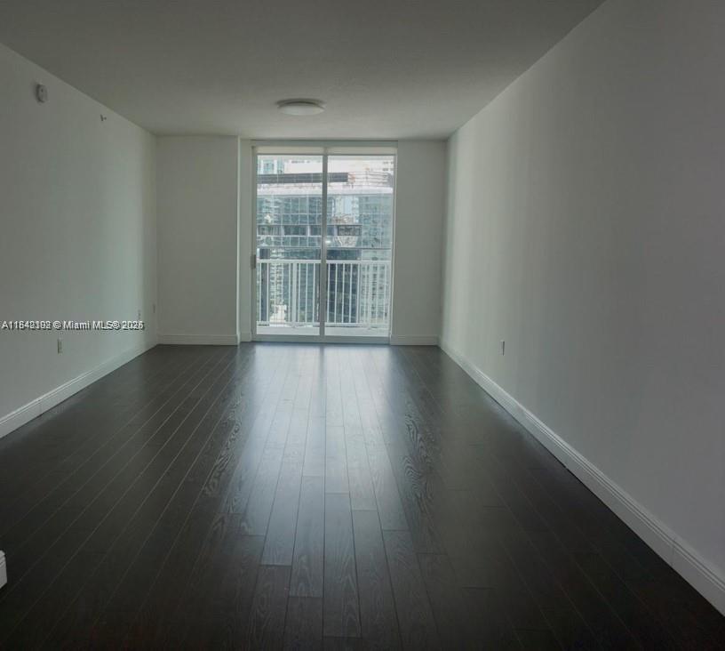 An empty room features dark wood flooring, white walls, and a sliding glass door to a balcony — 1250 S Miami Ave # 2006, Miami FL 33130, MIAMI, FL