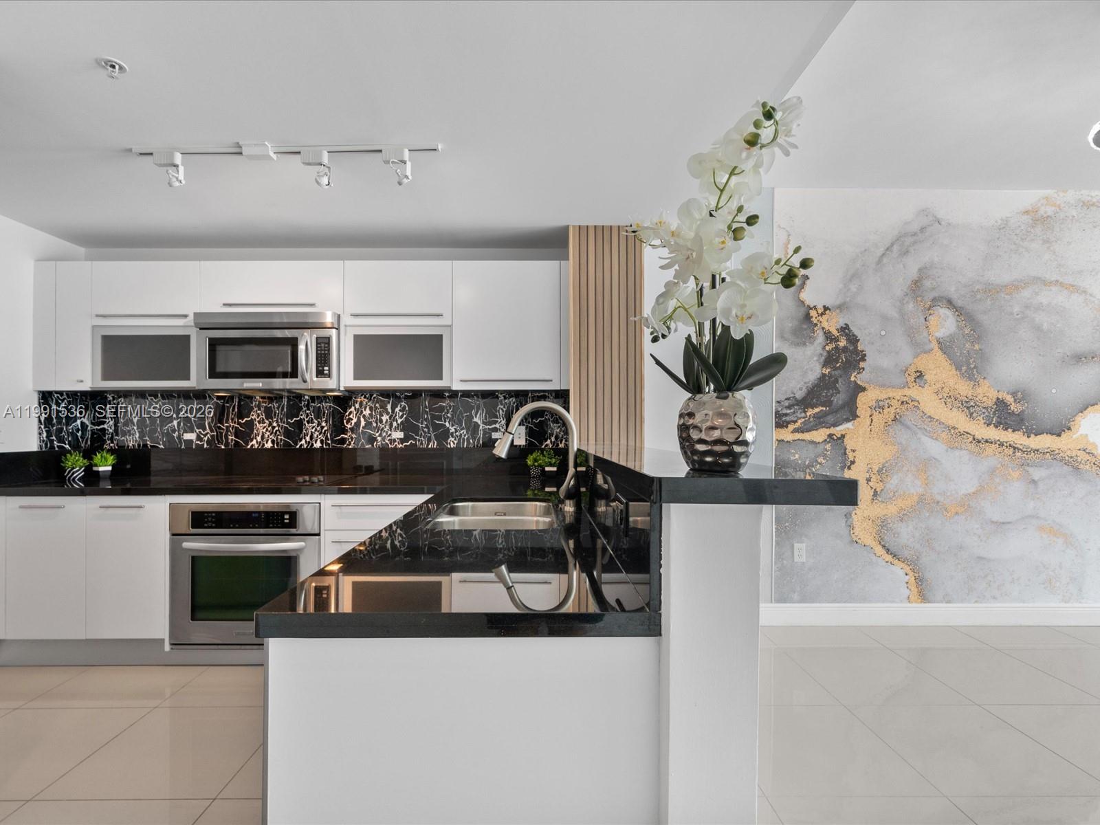 A modern kitchen features white cabinets, black marble countertops, and a decorative wall mural — 244 Biscayne Blvd # 1605, Miami FL 33132, MIAMI, FL