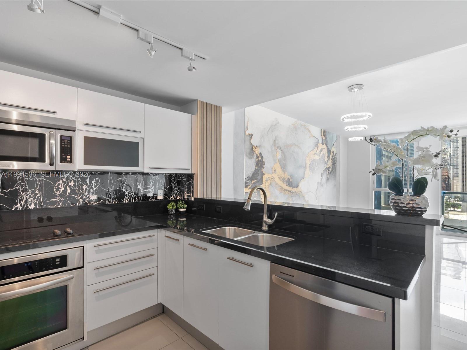 A modern kitchen features white cabinets, black marble backsplash, black countertops, and stainless steel appliances — 244 Biscayne Blvd # 1605, Miami FL 33132, MIAMI, FL