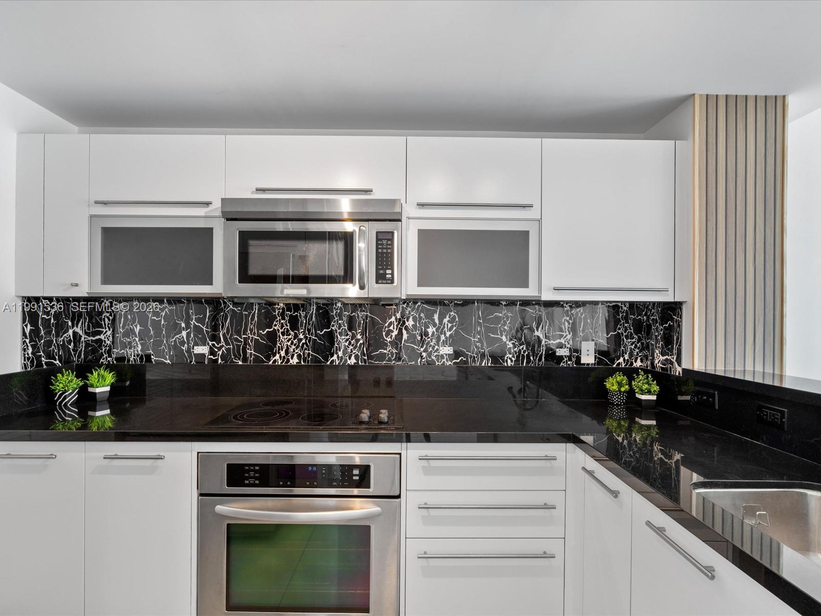 A kitchen features white flat-panel cabinets, black marble backsplash, and black granite countertops — 244 Biscayne Blvd # 1605, Miami FL 33132, MIAMI, FL