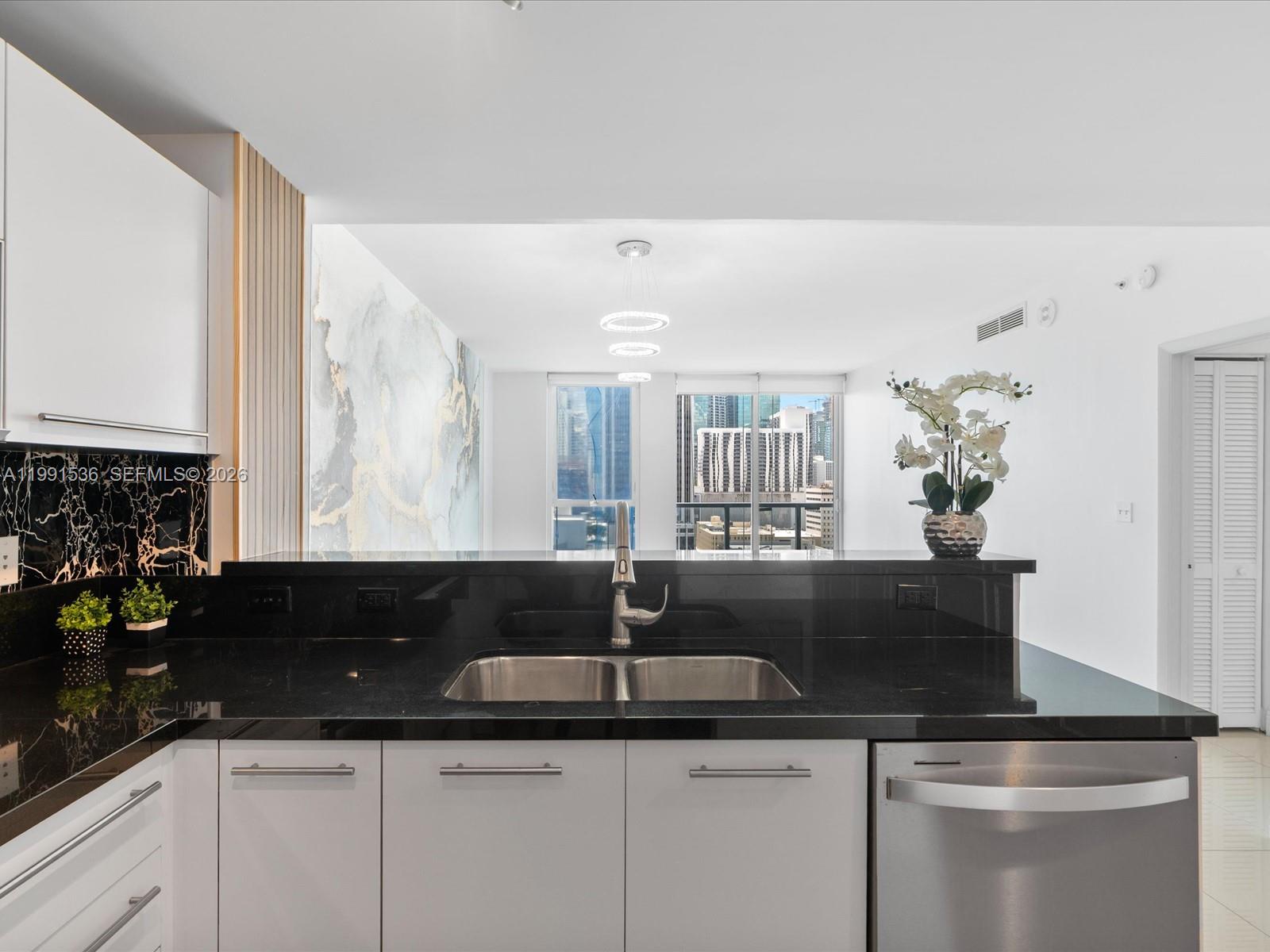 A kitchen with black countertops and white cabinets overlooks a living area with city views — 244 Biscayne Blvd # 1605, Miami FL 33132, MIAMI, FL