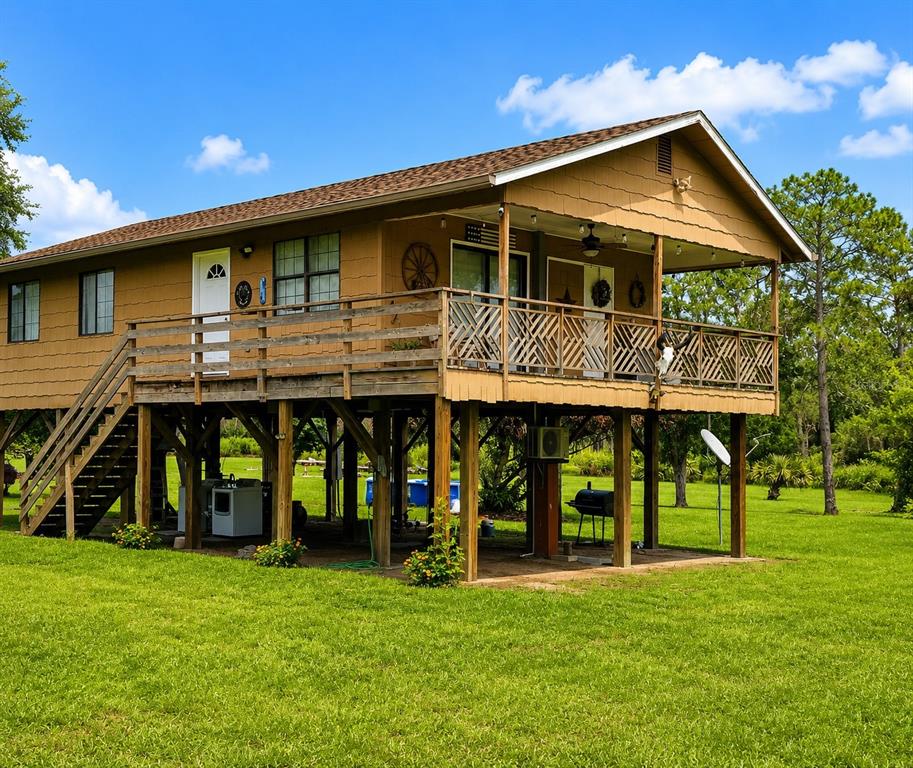 An elevated, tan-sided house with a wooden deck, stairs, and a grassy yard — 988 FAZZINI DR, FROSTPROOF, FL