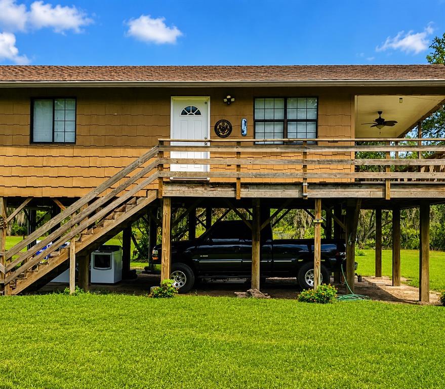 An elevated house with a wooden deck, stairs, and a black truck parked underneath — 988 FAZZINI DR, FROSTPROOF, FL