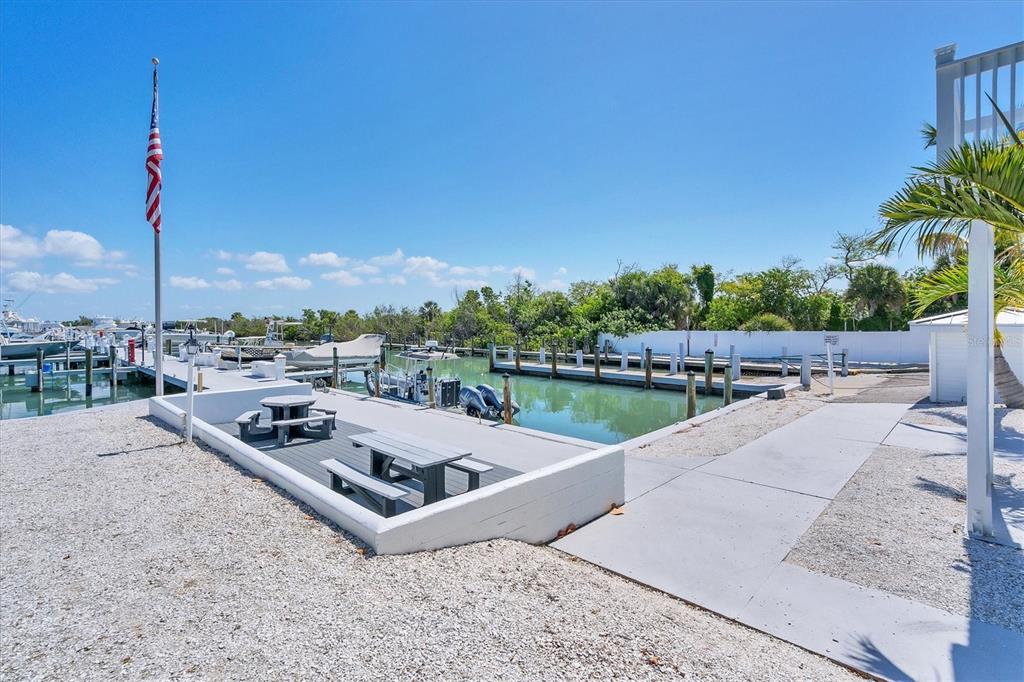 A concrete patio with picnic tables overlooks a boat slip and marina under a blue sky — 5820 GASPARILLA ROAD UNIT SLIP #49, BOCA GRANDE, FL