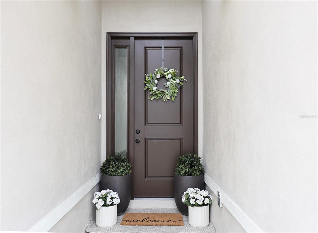 A dark brown front door with a side light, wreath, and potted plants on a porch — 7825 PINE GLEN ROAD, SEBRING, FL