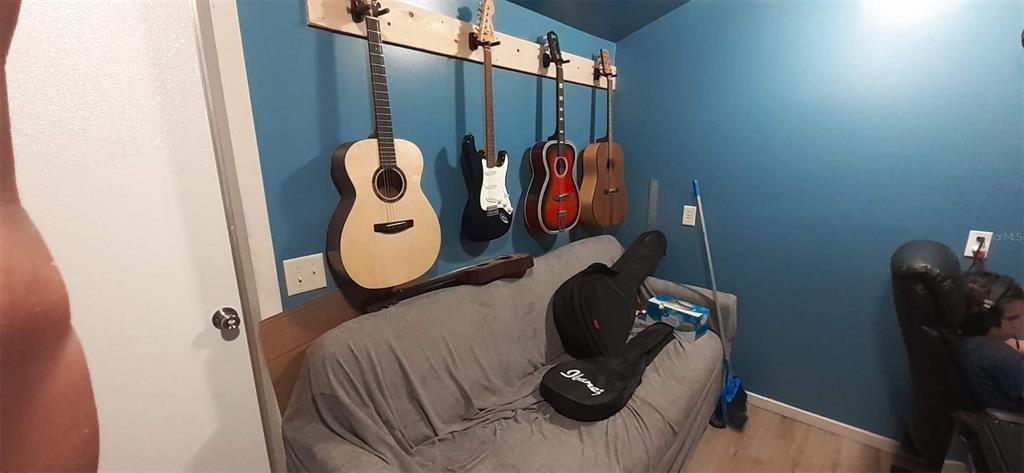 A room with blue walls features a sofa, a guitar wall rack, and several guitars — 2328 LIMEWOOD AVENUE UNIT 050, CLERMONT, FL
