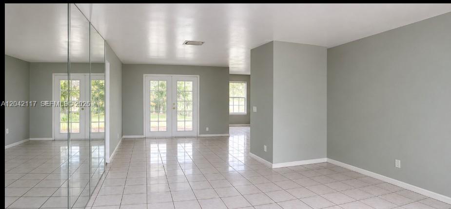 A bright, empty room features light-colored tile floors, mirrored closet doors, and French doors — ROYAL PALM BEACH, FL
