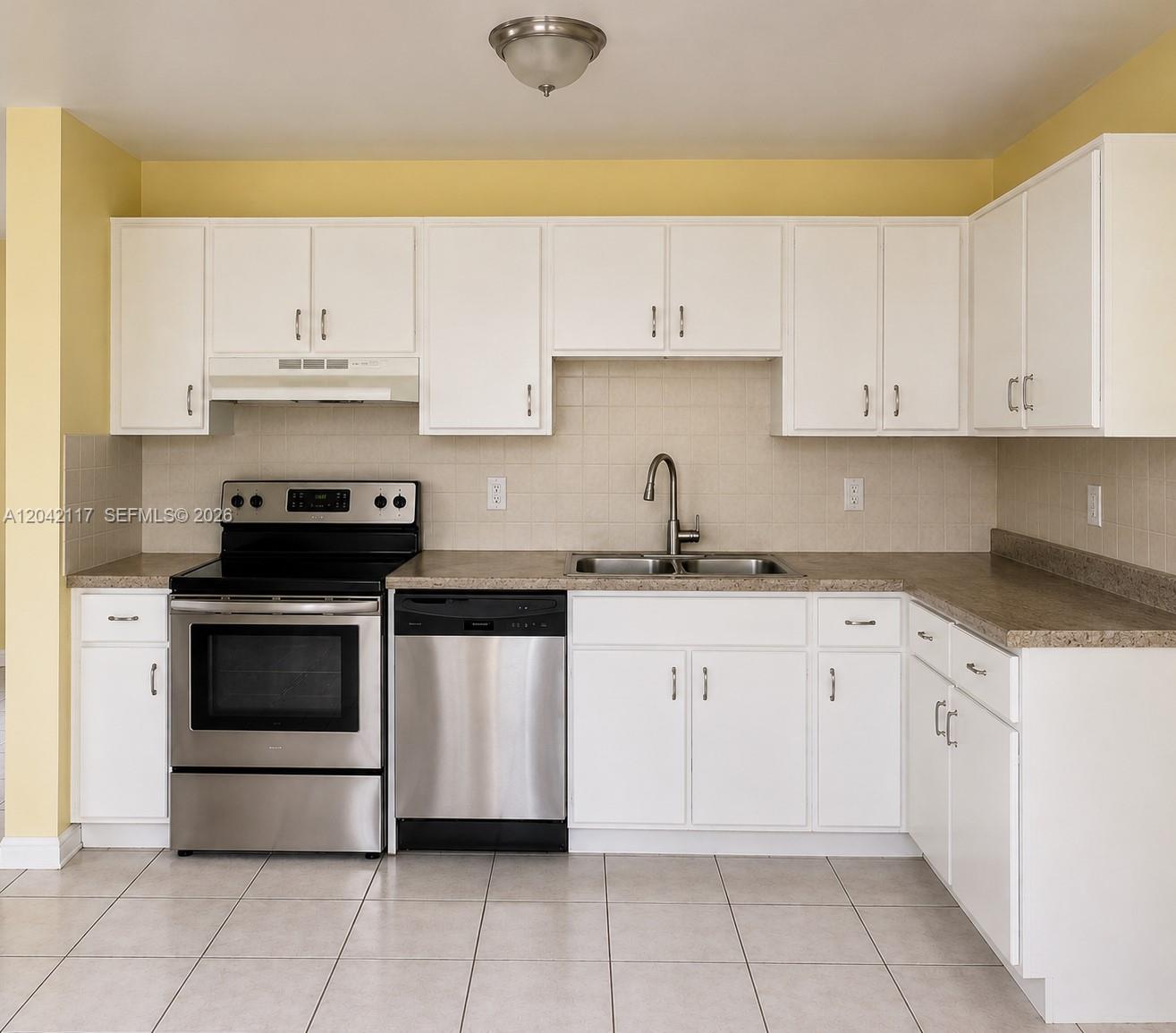 A kitchen features white cabinets, stainless steel appliances, a tile backsplash, and light-colored floor tiles — ROYAL PALM BEACH, FL